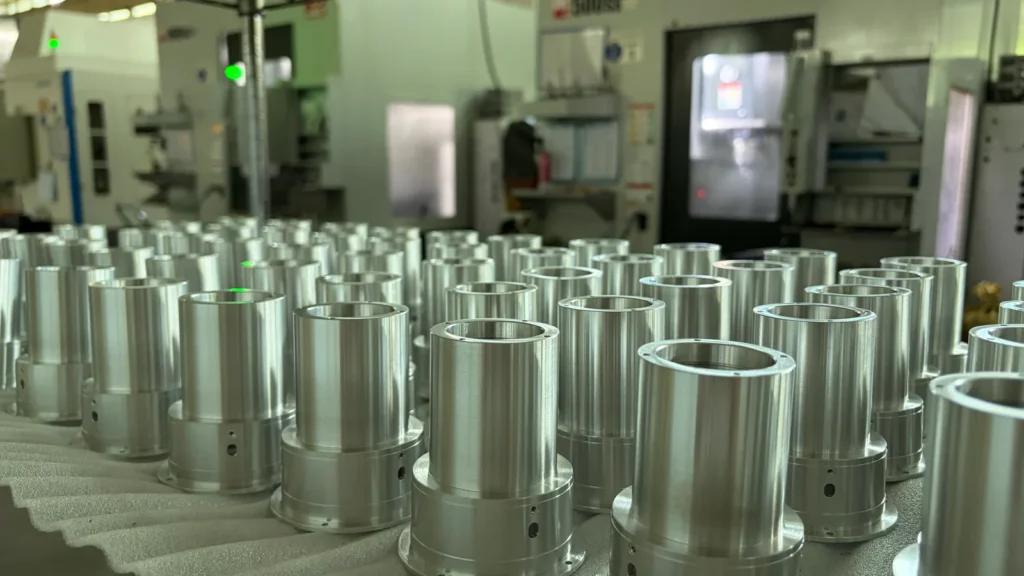 Rows of cylindrical metal components on foam with CNC machines in the background