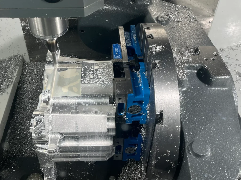 Tool holder and cutter beside a workpiece clamped in a blue vise on a five-axis CNC machine