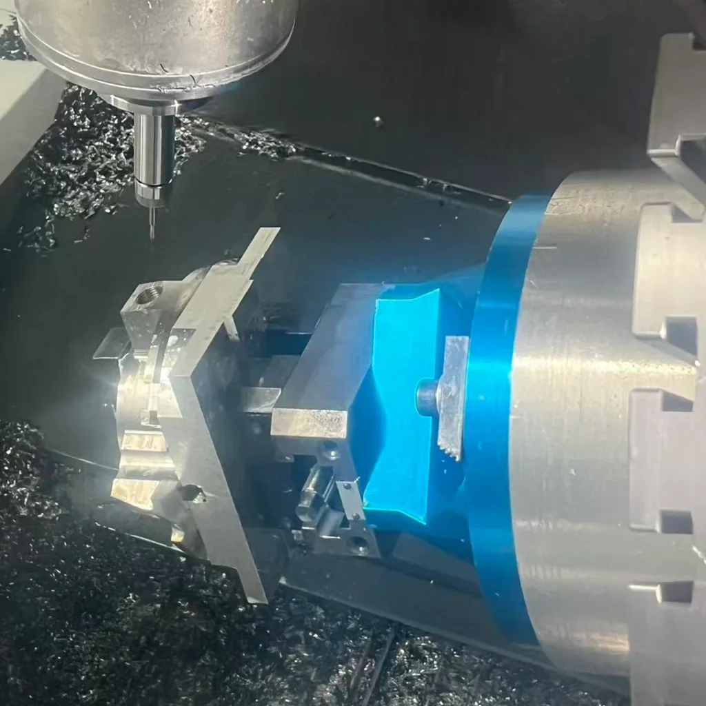 Slim cutting tool above a workpiece held beside a blue fixture on a five-axis CNC machine