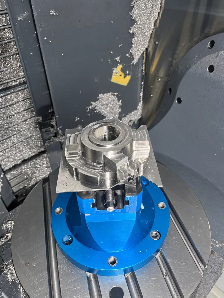 Titanium workpiece with a central bore secured in a blue CNC fixture