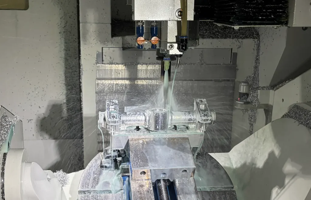 Five-axis CNC machining of an aluminum workpiece with the spindle, fixture and rotary table visible