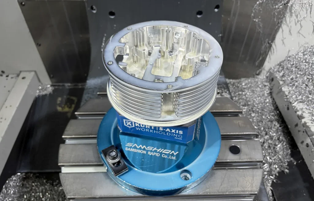Aluminum CNC part mounted on a five-axis workholding fixture inside a machining center