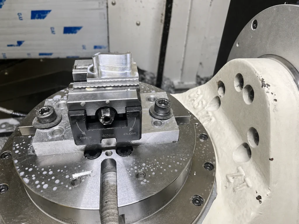 As-machined aluminum part held in a vise on a rotary table for multi-axis CNC milling