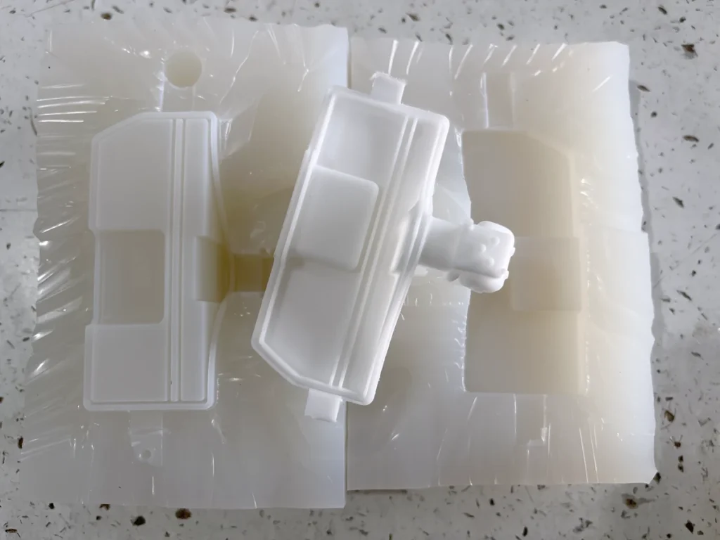 White vacuum cast part resting on an opened silicone mold with a matching cavity