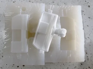 White vacuum cast part resting on an opened silicone mold with a matching cavity
