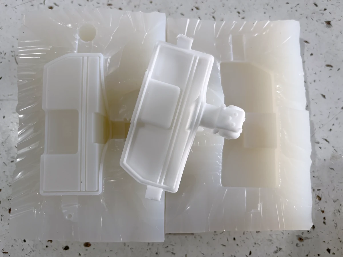 White vacuum cast part resting on an opened silicone mold with a matching cavity