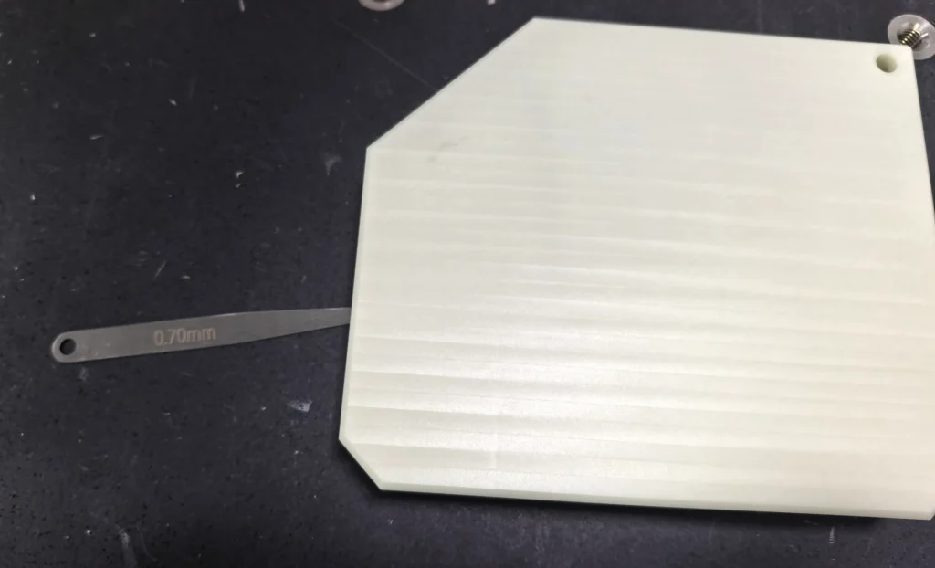 Feeler blade marked 0.70 mm inserted beneath a CNC machined ABS part on a measuring platform
