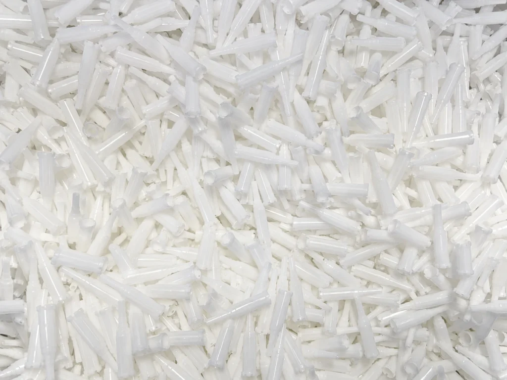 A large batch of white plastic components with slender tubular shapes.