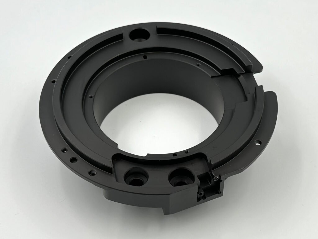Black-anodized 6061-T6 aluminum ring-shaped component with stepped surfaces and mounting holes.