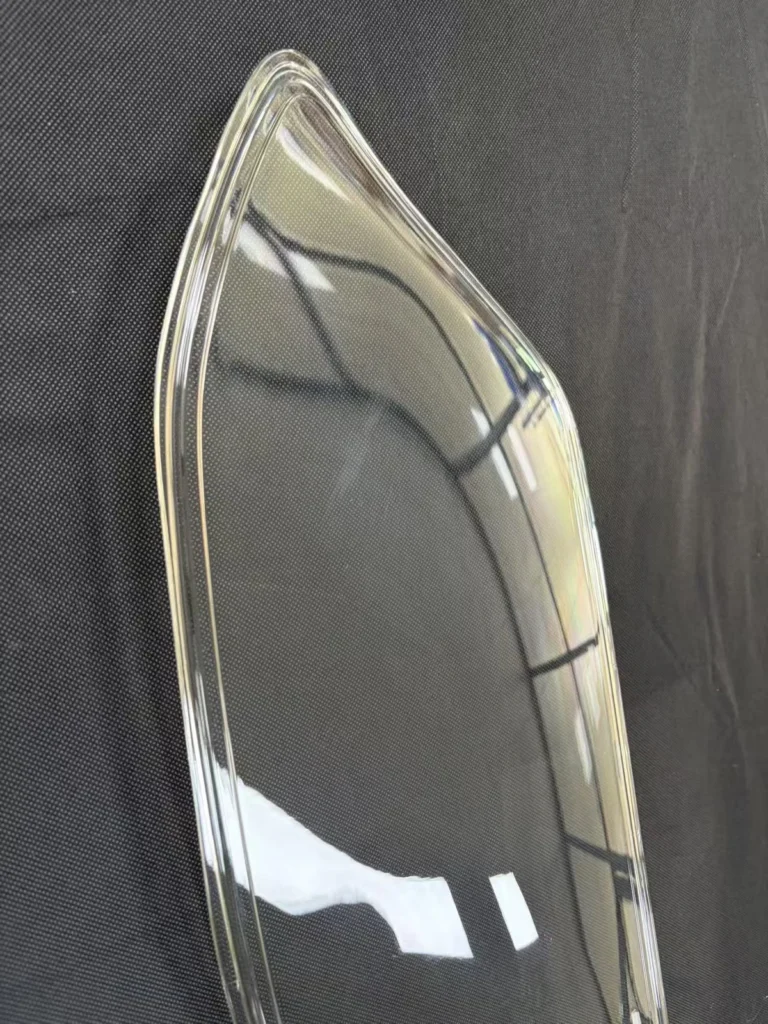 Close-up of a clear PC automotive lamp cover showing its curved surface and perimeter edge
