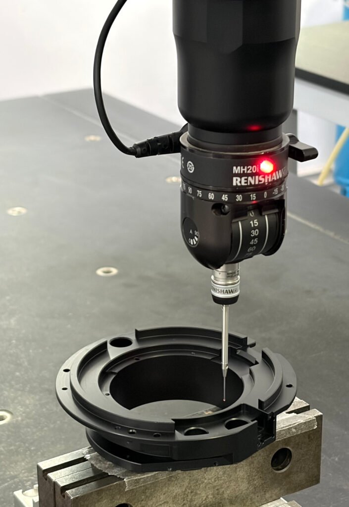 CMM probe positioned over a black-anodized 6061-T6 aluminum ring-shaped component held in a fixture.