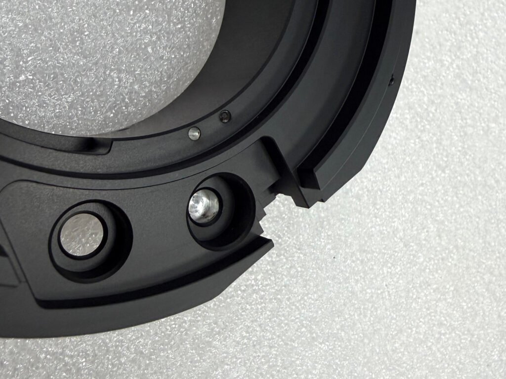 Close-up of holes, a threaded hole and circumferential grooves on a black-anodized aluminum ring.