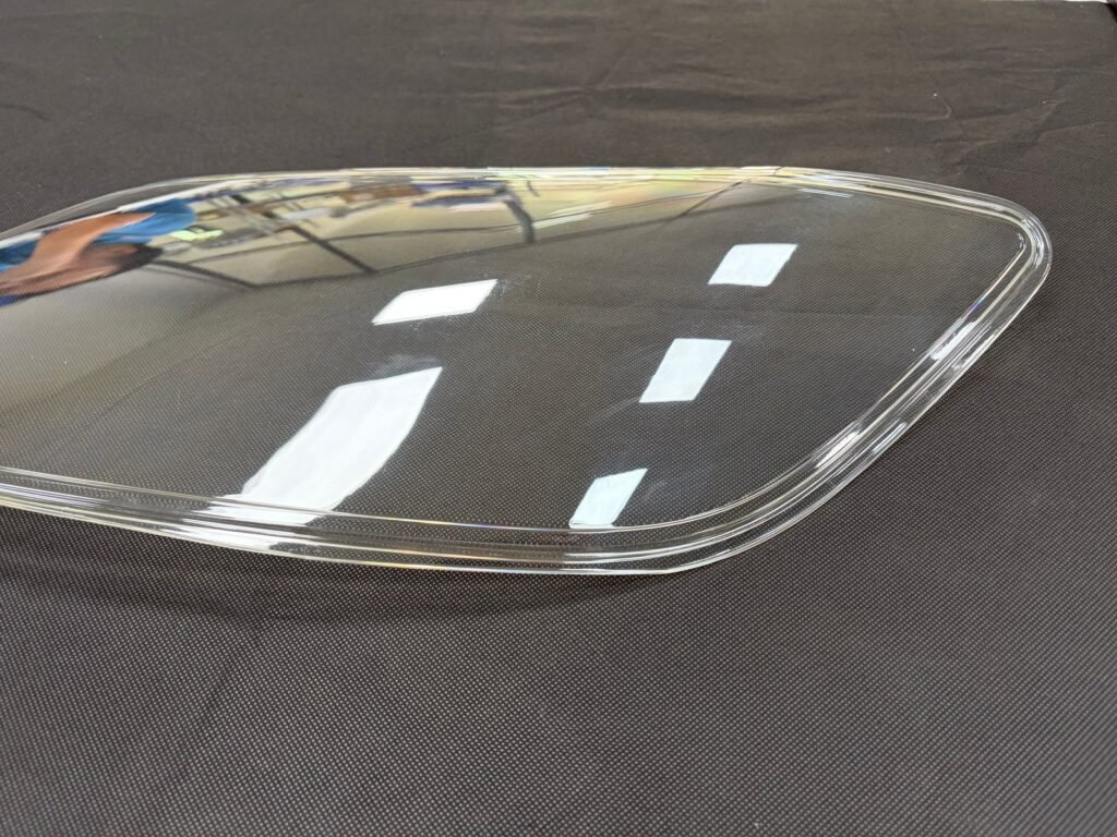 Transparent PC automotive lamp cover with a curved surface and raised perimeter edge on a dark background