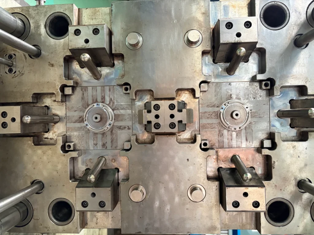 Close-up of an injection mold showing steel plates, circular inserts, angled pins and slide blocks.