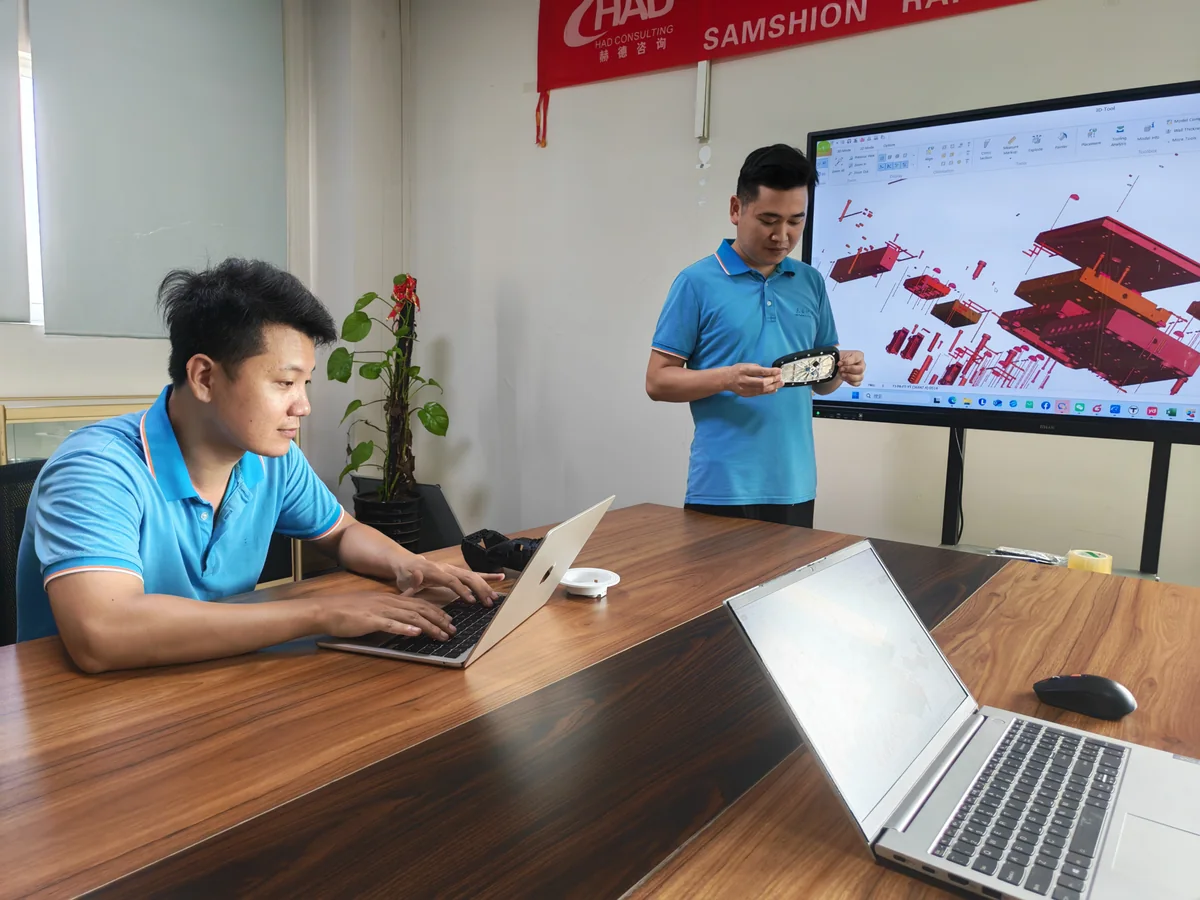 SAMSHION team reviewing a mold design on screen and a molded component during an engineering discussion.