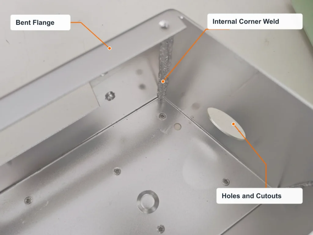 Sheet metal enclosure detail with labels identifying a bent flange, an internal corner weld and a side cutout.