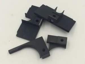 Four black oxide finished machined components with semicircular cutouts and holes