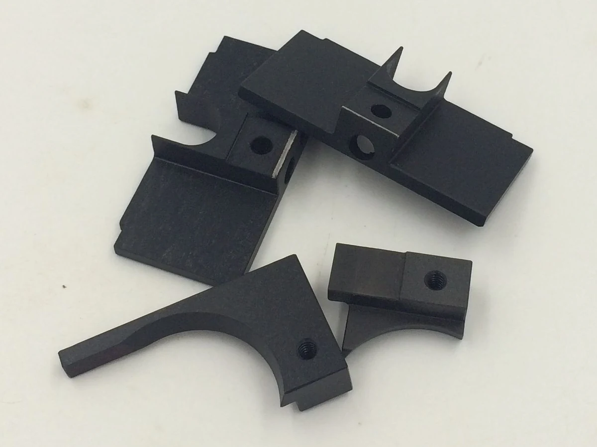 Four black oxide finished machined components with semicircular cutouts and holes
