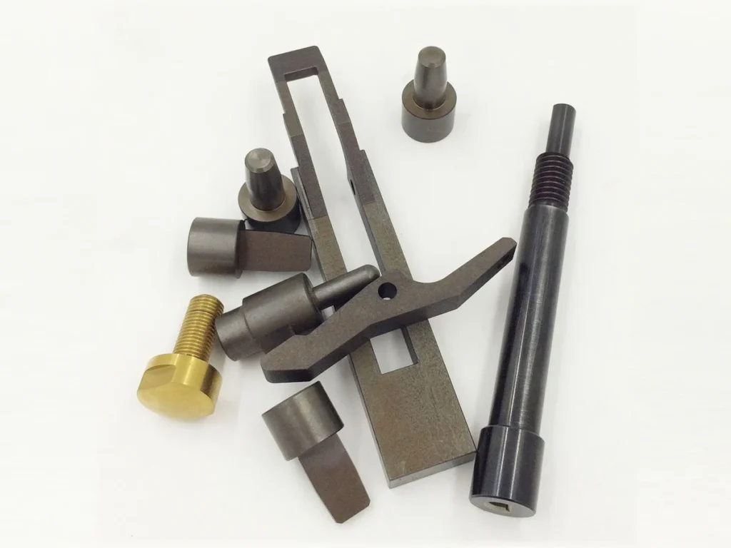 Black oxide finished machined components with a slotted frame and threaded shaft, alongside a gold-colored fastener