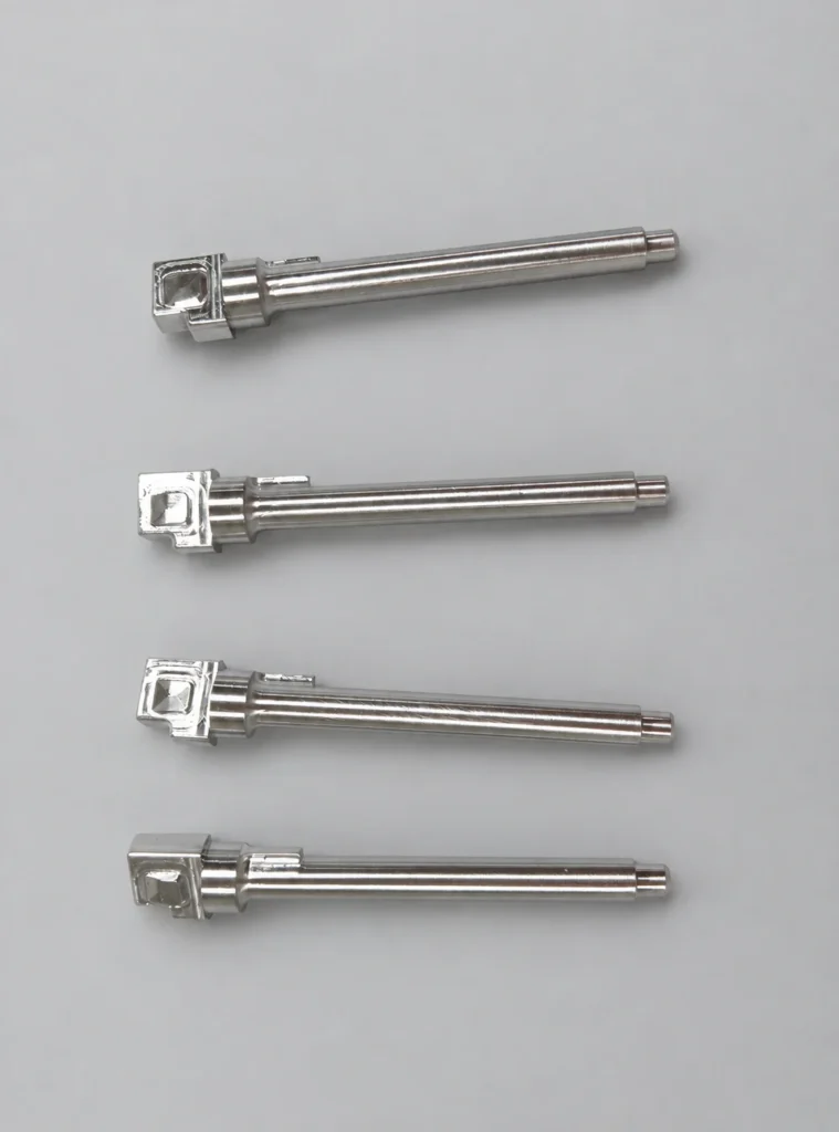 Four machined shaft components with long cylindrical bodies and enlarged end features