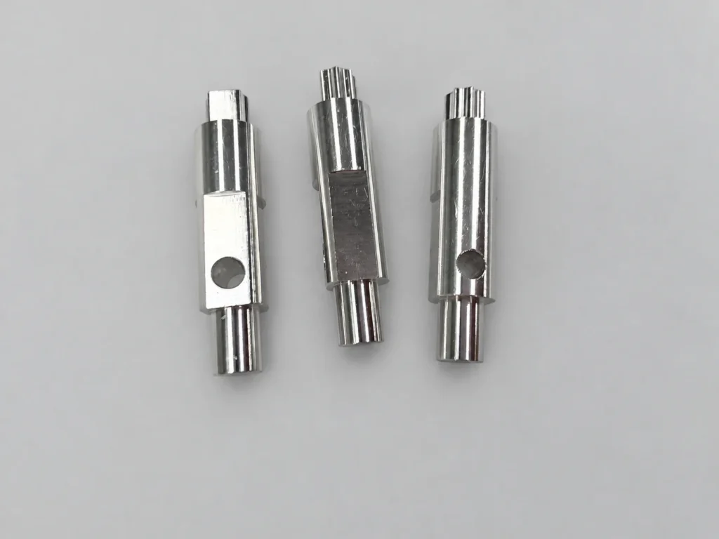 Three small machined shaft components with stepped diameters, flats and transverse holes