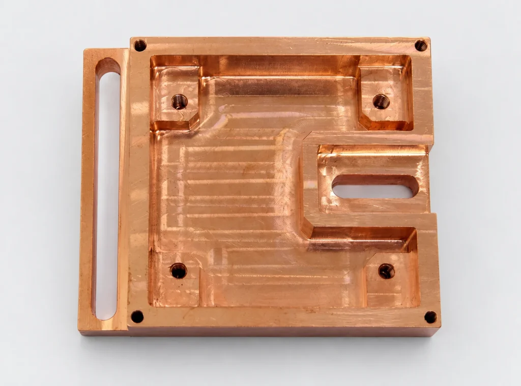 Copper component milled from solid stock with a pocket, elongated slots and threaded holes